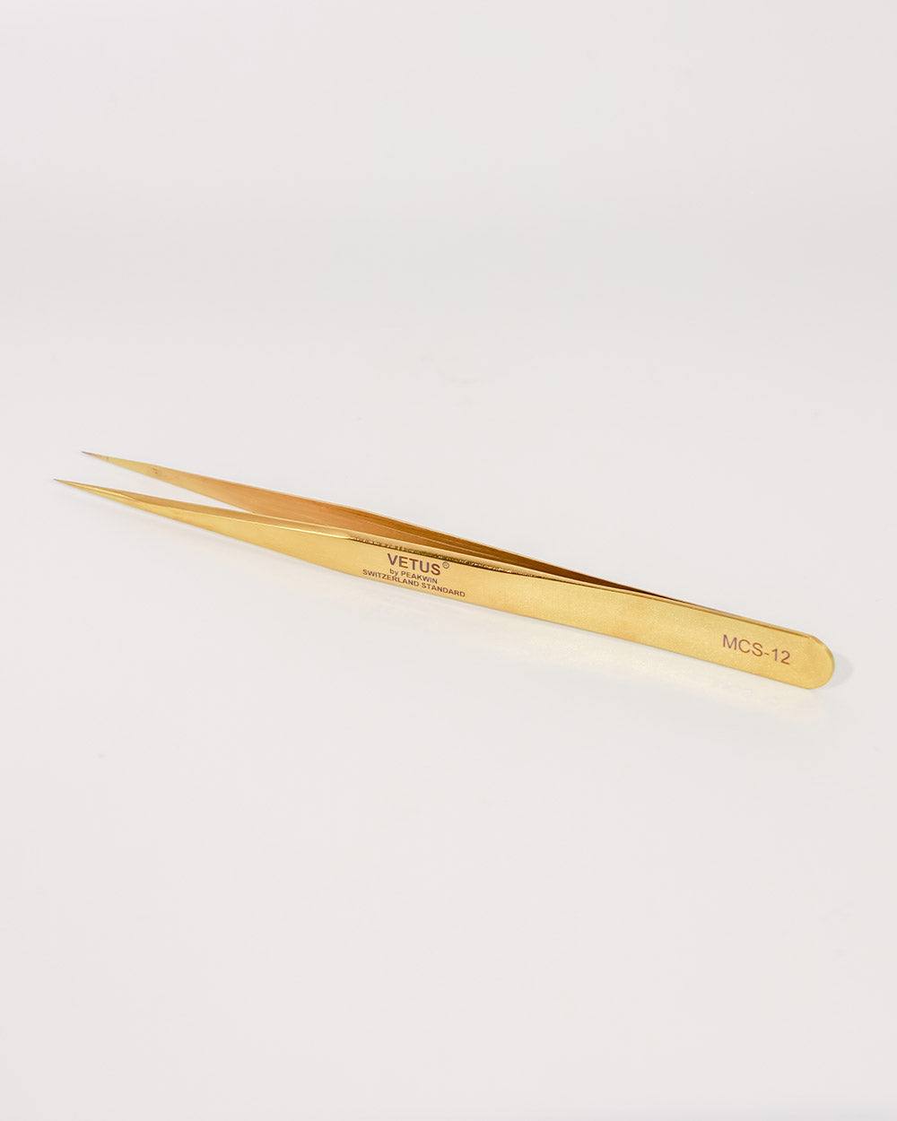 Gold-colored tweezers on a light gray background