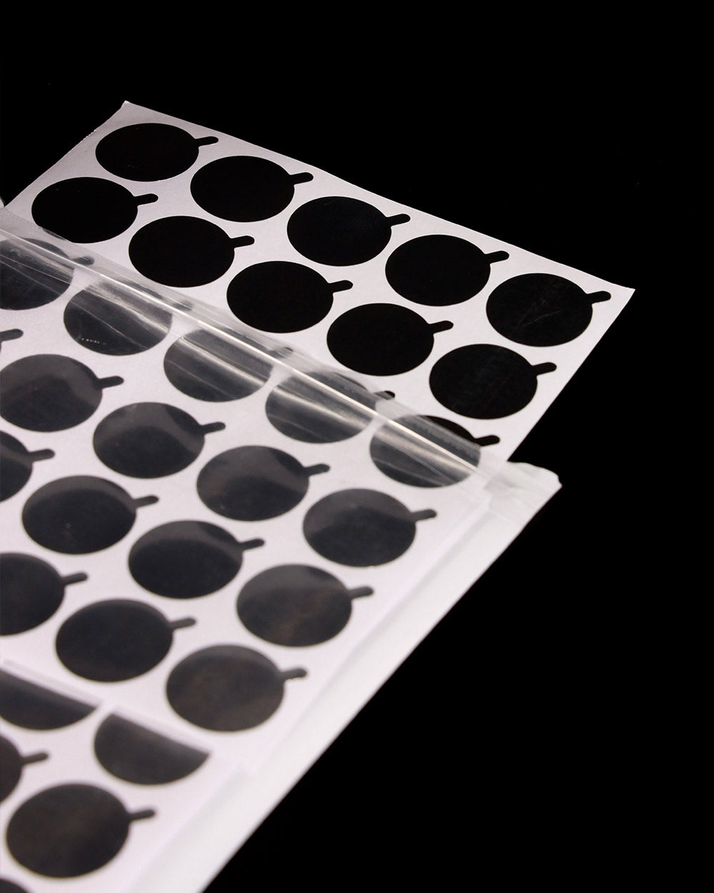 Sheet of black oval stickers on a clear plastic sheet against a black background